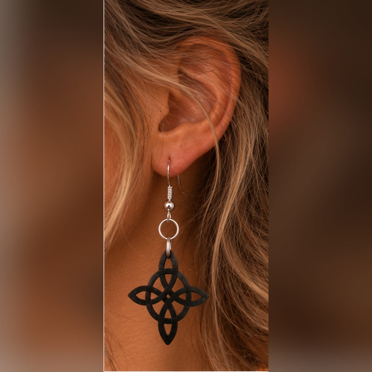Close-up of a black Celtic knot dangle earring with silver fishhook finding, showing the intricate interwoven design and lightweight hanging style.