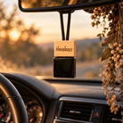 Abundance refillable car diffuser hanging from rearview mirror with laser-engraved wooden cap and black glass fragrance bottle.