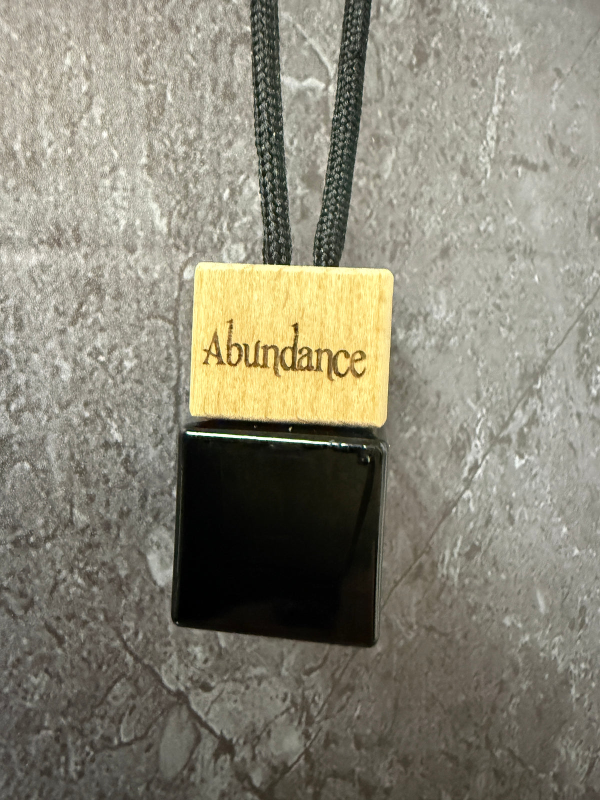Close up of Wildwood Ritual Abundance 8ml glass car diffuser with engraved wooden cap and adjustable black hanging cord.
