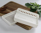 White soap dish with 'Wildwood & Lather' branding on a wooden tray with cinnamon sticks and a plant in the background.