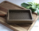 Dark Brown 3D printed soap dish on a wooden cutting board with cinnamon sticks and green leaves in the background