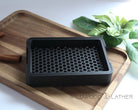 Black 3D printed soap dish on a wooden cutting board with cinnamon sticks and green leaves in the background