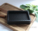 Black 3D printed soap dish on a wooden cutting board with cinnamon sticks and green leaves in the background